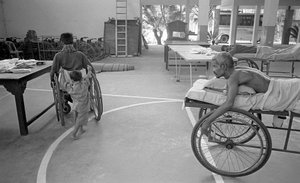 Een lichamelijk gehandicapte man in een rolstoel wordt gedragen door zijn zoon; een andere man met hetzelfde lot kijkt toe in het Centrum voor Revalidatie van Verlamden, CRP in Savar, Dhaka, Bangladesh. 2005. door Unbekannt Unbekannt